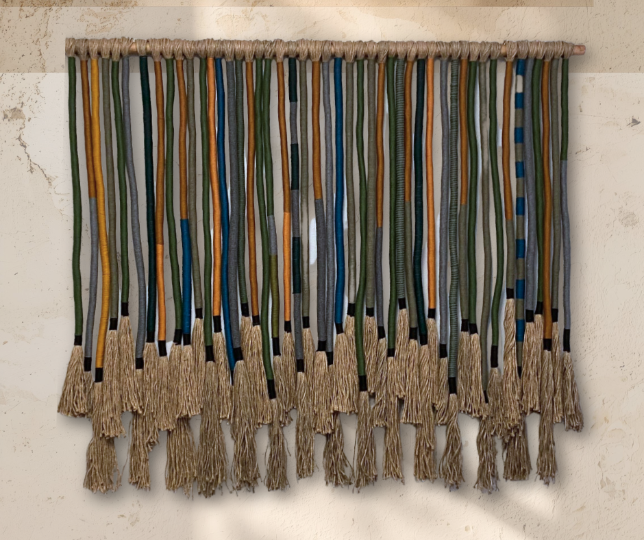 Woven wall hanging with colorful strips and fringes on a beige wall.